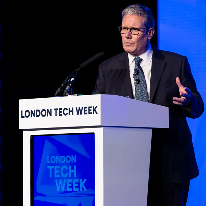 Sir Kier Starmer speaking at a podium with microphones during London Tech Week 2026, with a blue background, at Olympia.