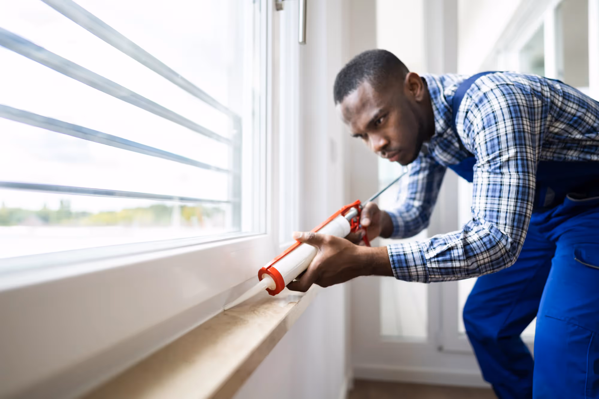 A repairman applying sealant to a window.