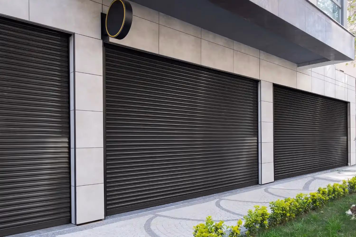 Three modern, black garage doors with horizontal slats are closed on a building.