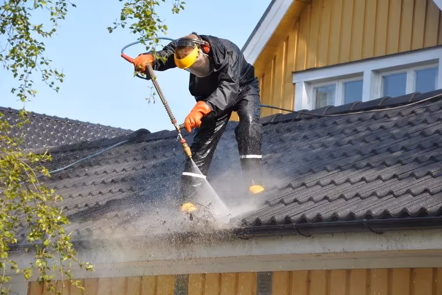 A person power washing debris from a gutter.