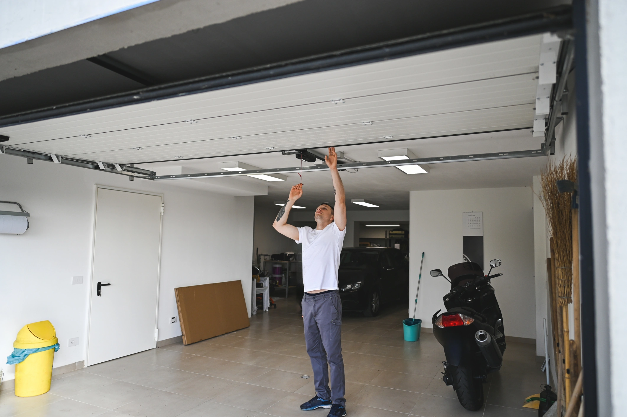 Man in a garage repairing the mechanism of an automatic overhead garage door.