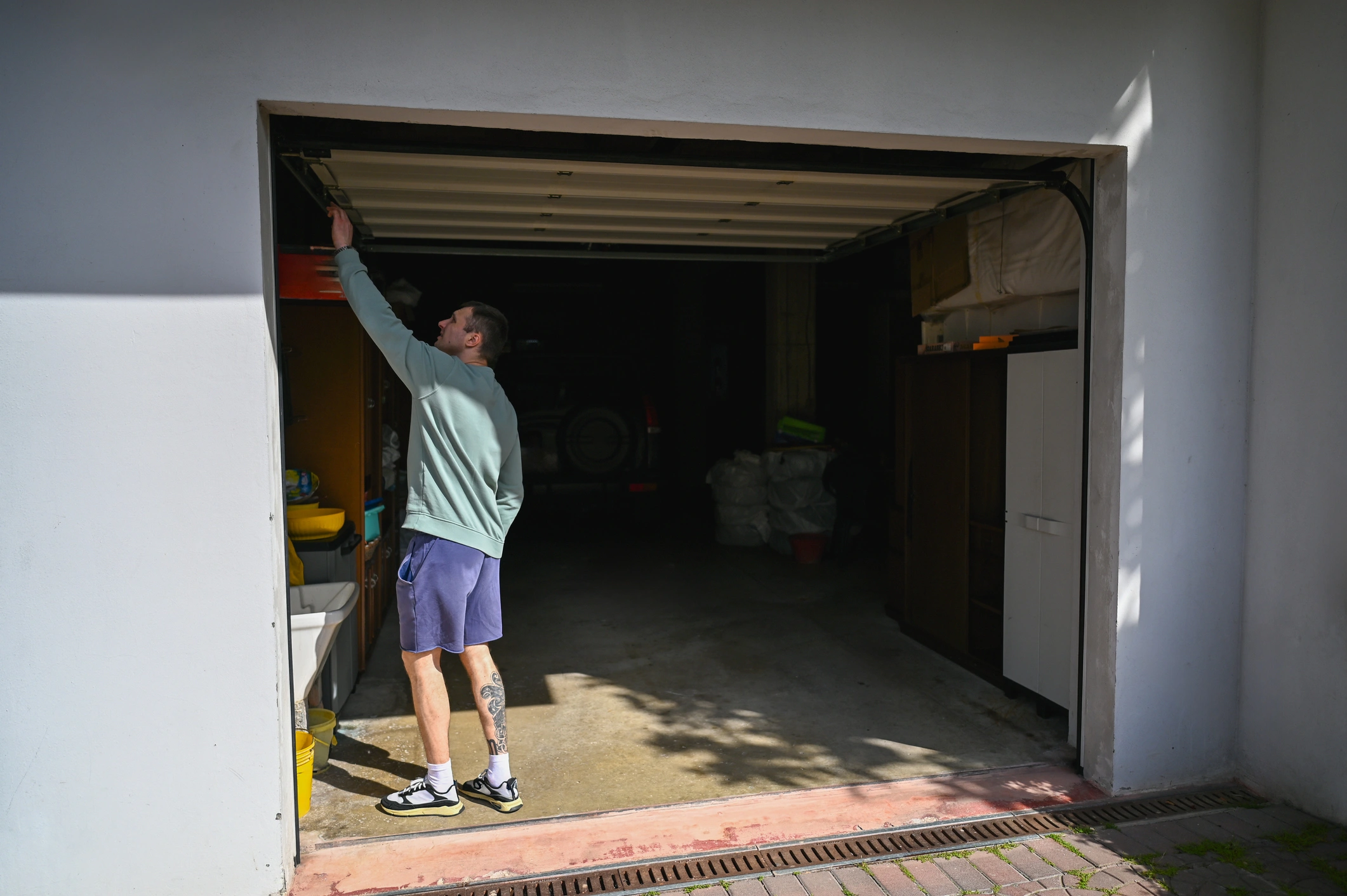 Man in shorts adjusting the track of an open automatic garage door on a sunny day.