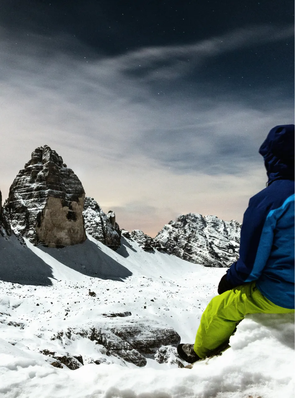 Bergsteiger steht auf Felsen mit Blick auf zerklüftete Bergspitzen
