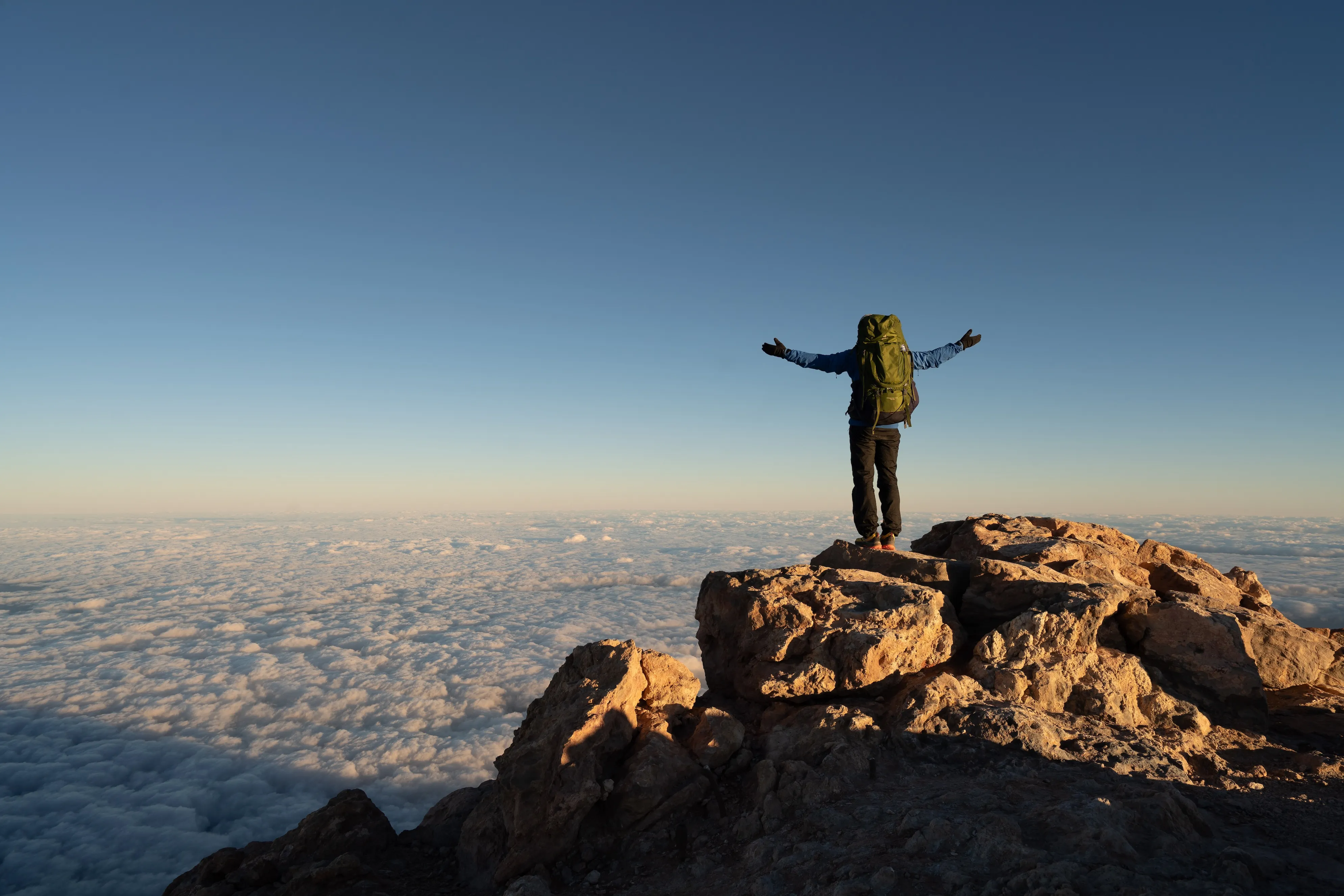 Person steht mit ausgestreckten Armen auf Gipfel über Wolkenmeer