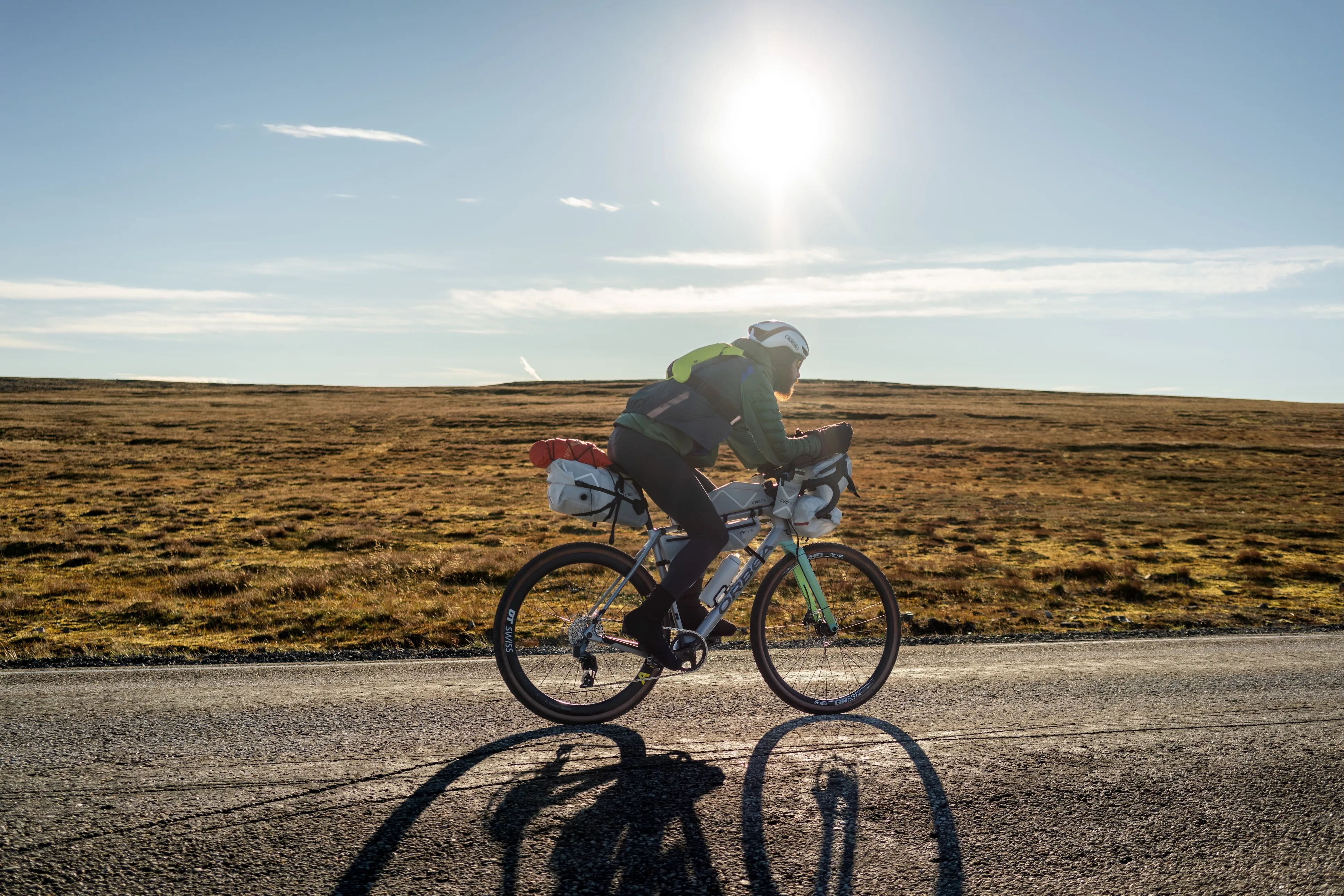 Radfahrer fährt auf ebener Straße im Gegenlicht der tief stehenden Sonne