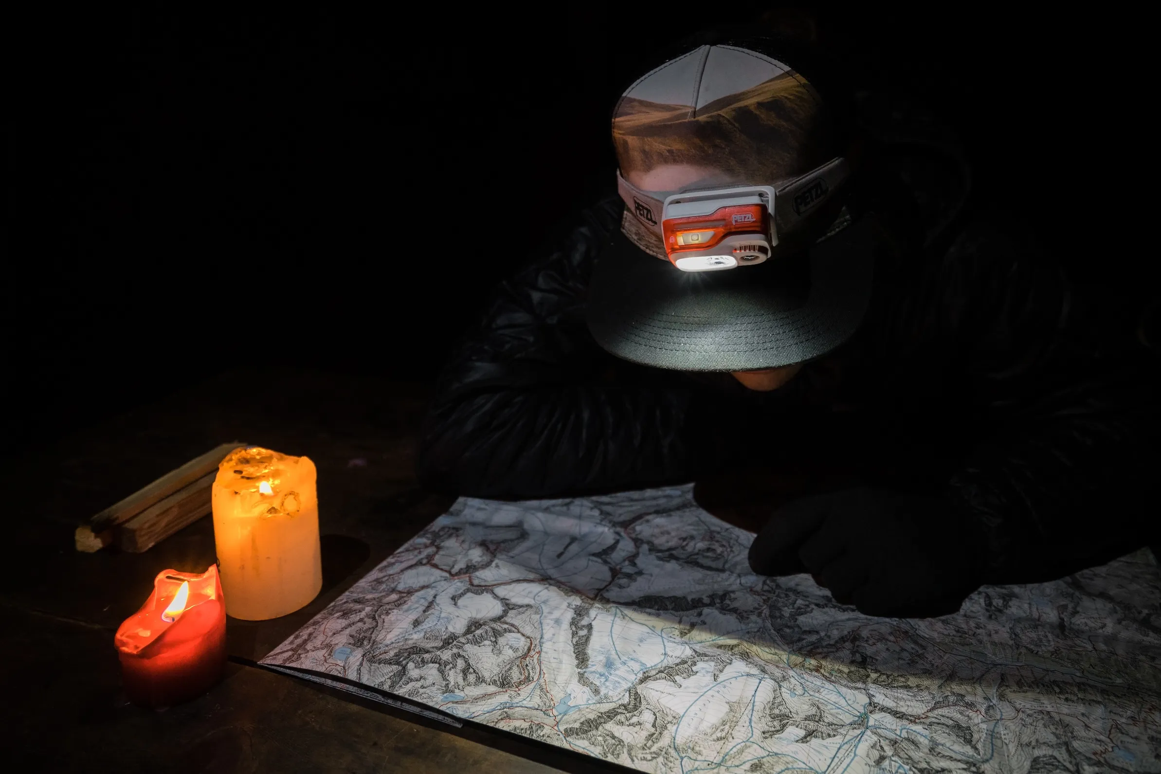 Person liest bei Kerzenlicht an einem Tisch eine Landkarte