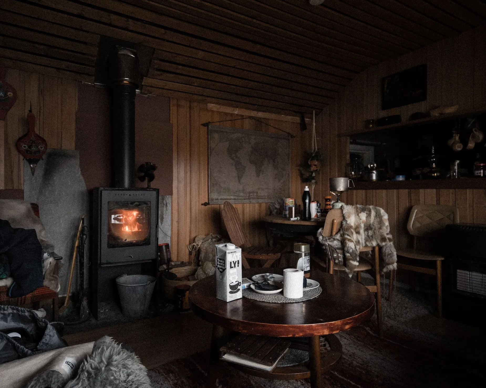 Gemütlicher Innenraum einer Hütte mit Kamin, Stühlen, Hafermilch und Tisch