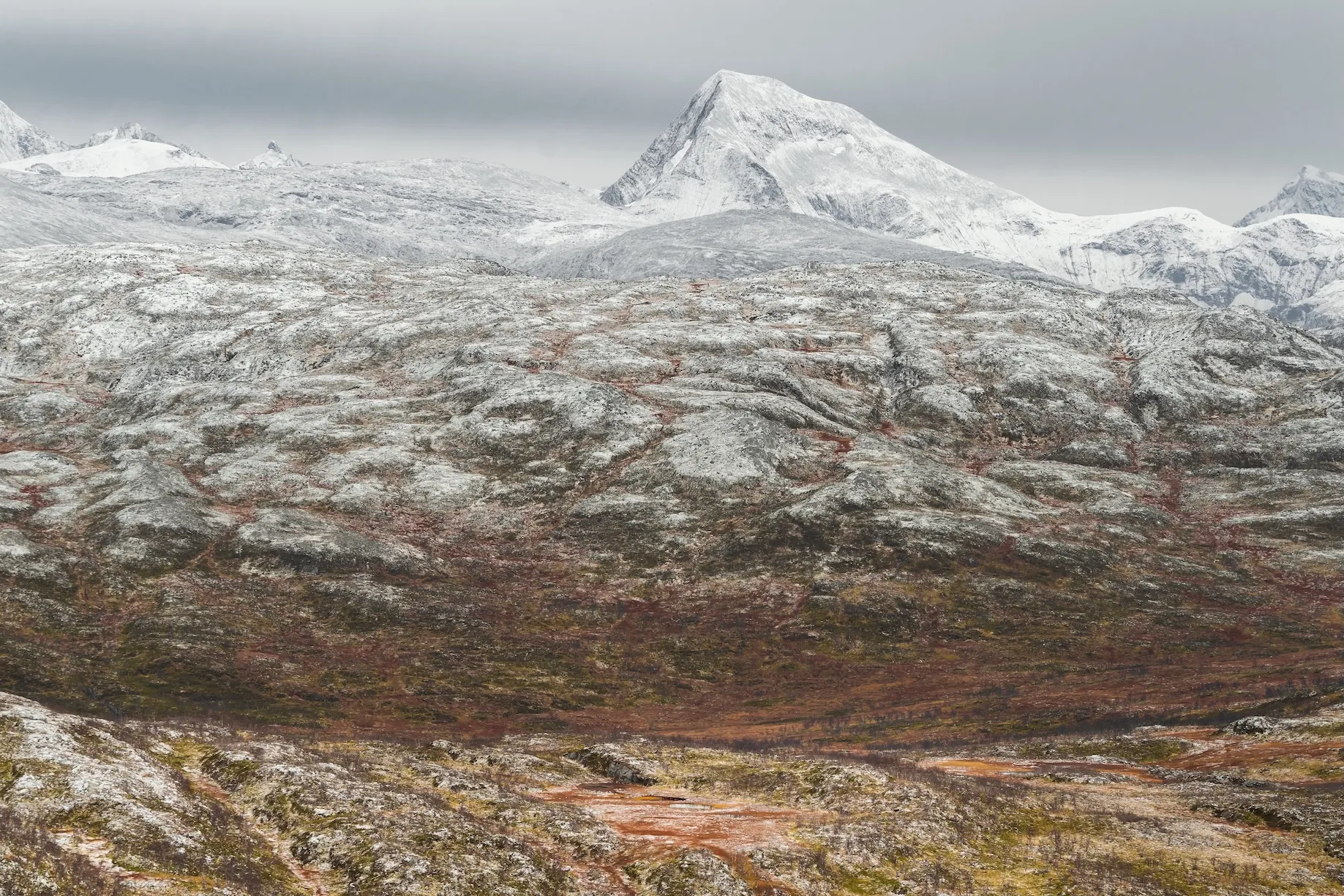 Schneebedecktes Bergpanorama mit wolkigem Himmel und herbstlicher Landschaft in Skandinavien