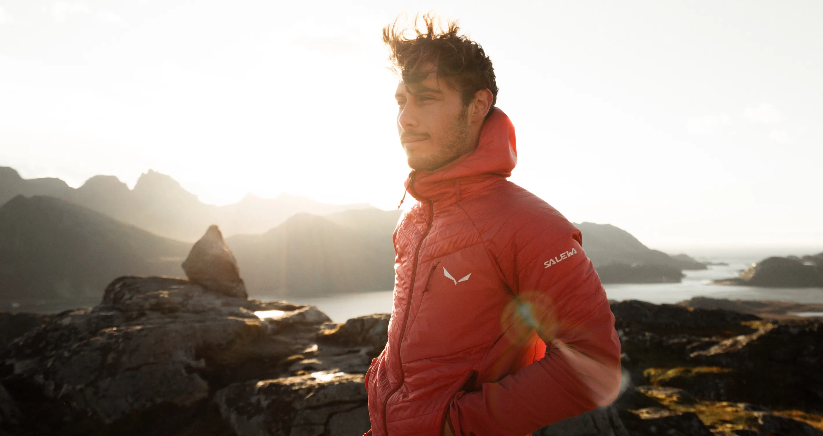 Person in rotem Jacket steht auf Felsen mit Blick auf das Meer
