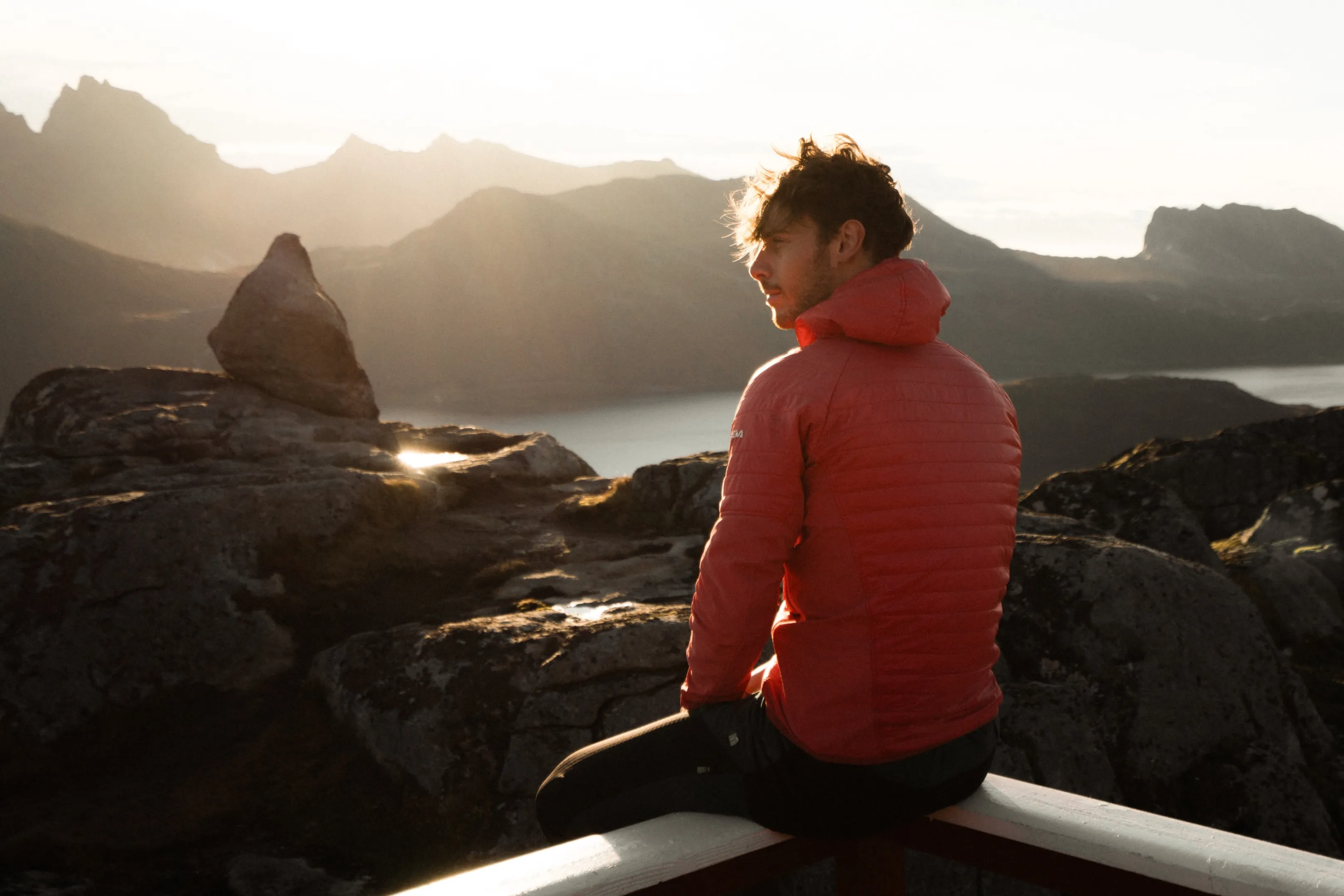 Person sitzt auf einem Geländer am Meer bei Sonnenaufgang