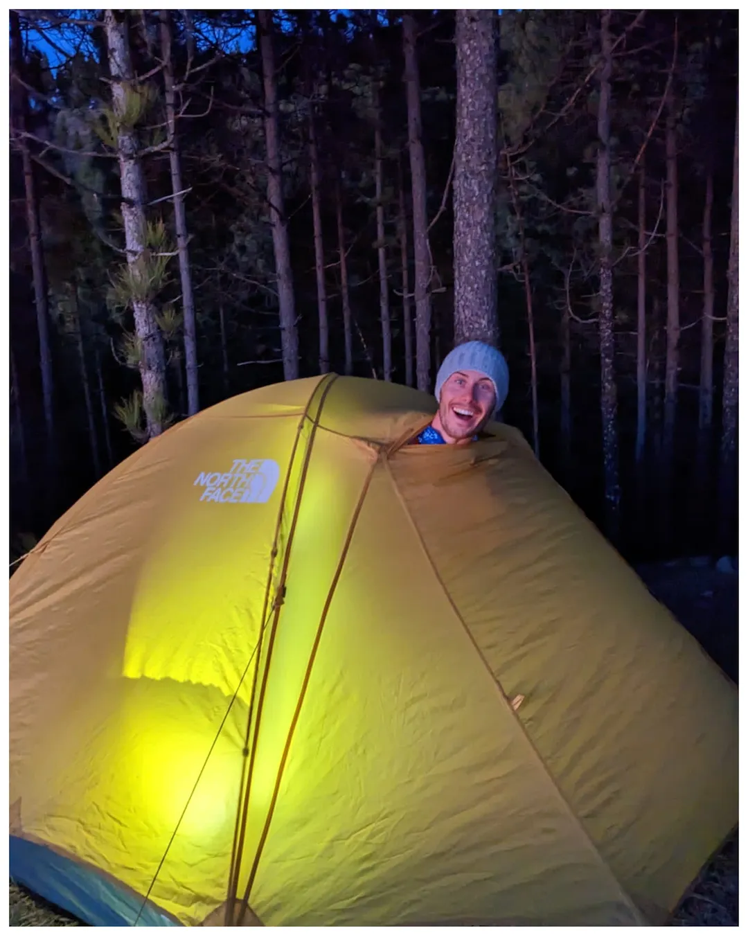 Person lacht aus Zelt in einem Wald in der Nacht, Licht leuchtet aus dem Inneren