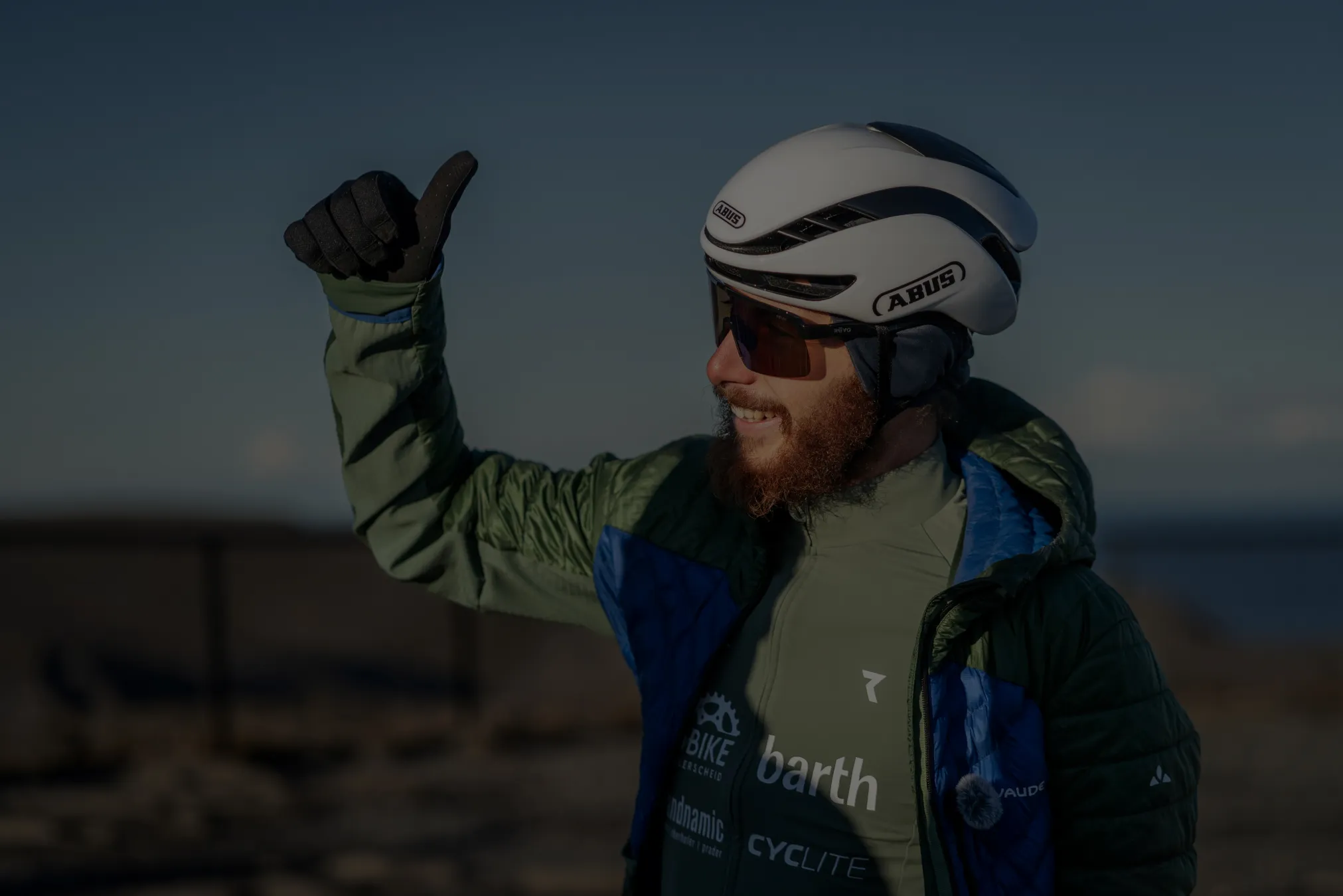 Stefan mit weißem Rad-Helm und Sponsoren-Trikot, grinst und winkt nach einem langen Lauftag während Crossing Europe Twice