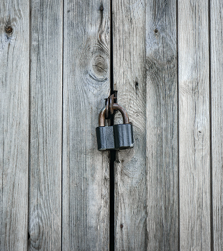 Black padlock securing two weathered wooden boards with visible knots and grain.