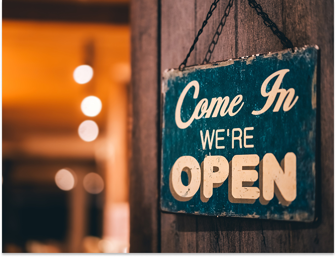 Rustic blue wooden sign hanging on a dark wood wall with the text 'Come In We're OPEN'.