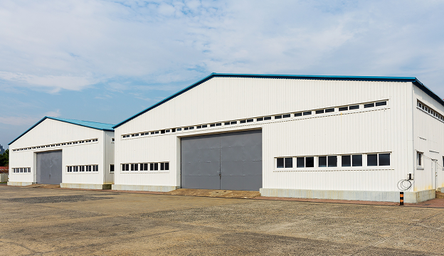 Two large white industrial warehouses with blue roofs and gray doors under a partly cloudy sky.