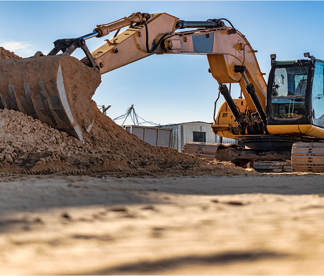 Yellow excavator digging and moving a large pile of dirt at a construction site under a clear blue sky.
