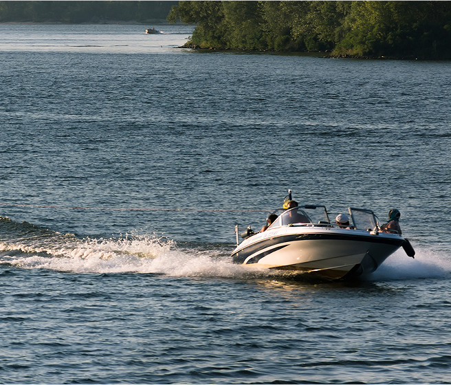 Speedboat with four people cruising on a calm lake near a tree-lined shore.