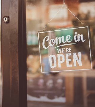 Glass door with a hanging sign that reads 'Come in, we're OPEN.'