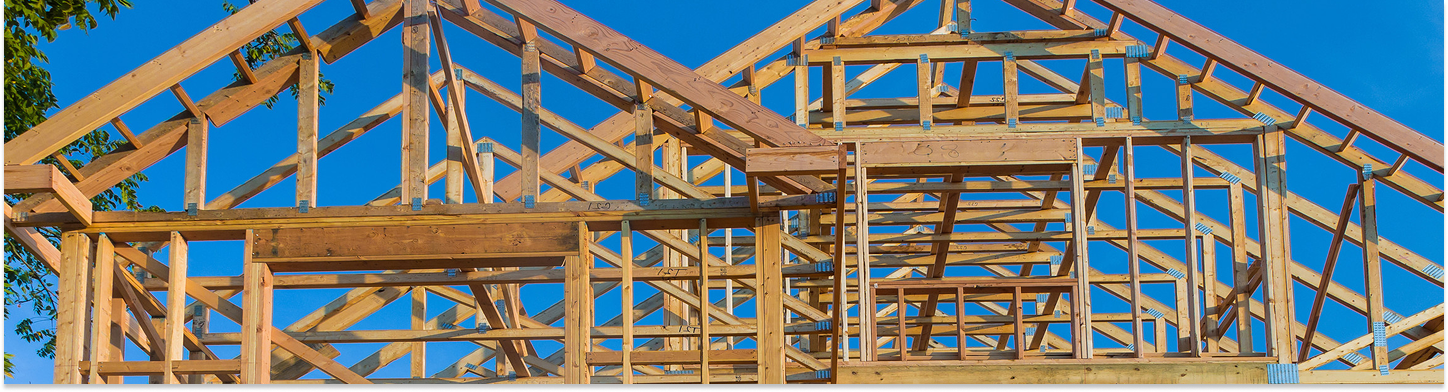 Wooden frame structure of a house under construction against a clear blue sky.