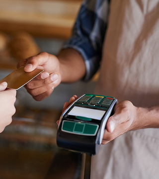 Person holding a payment terminal while another person presents a credit card for contactless payment.