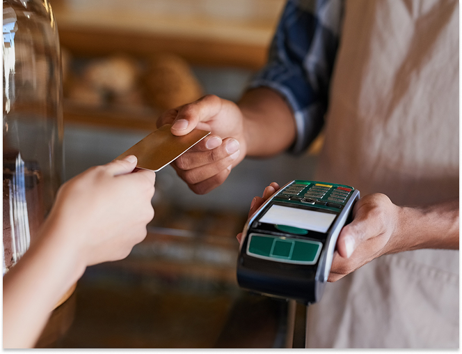 A cashier holding a payment terminal while a customer hands over a credit card for payment.