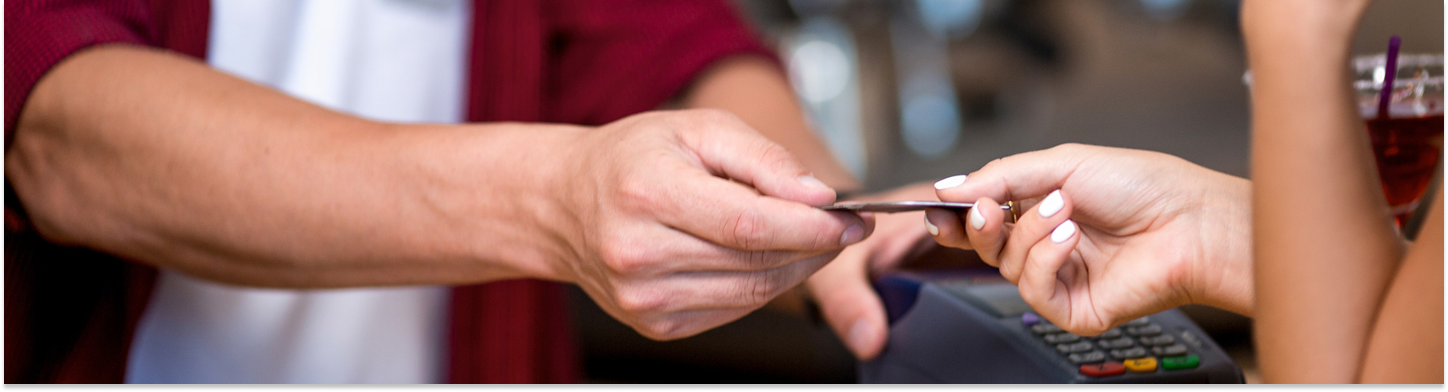 A person holding a credit card handing it to another person near a card payment terminal.