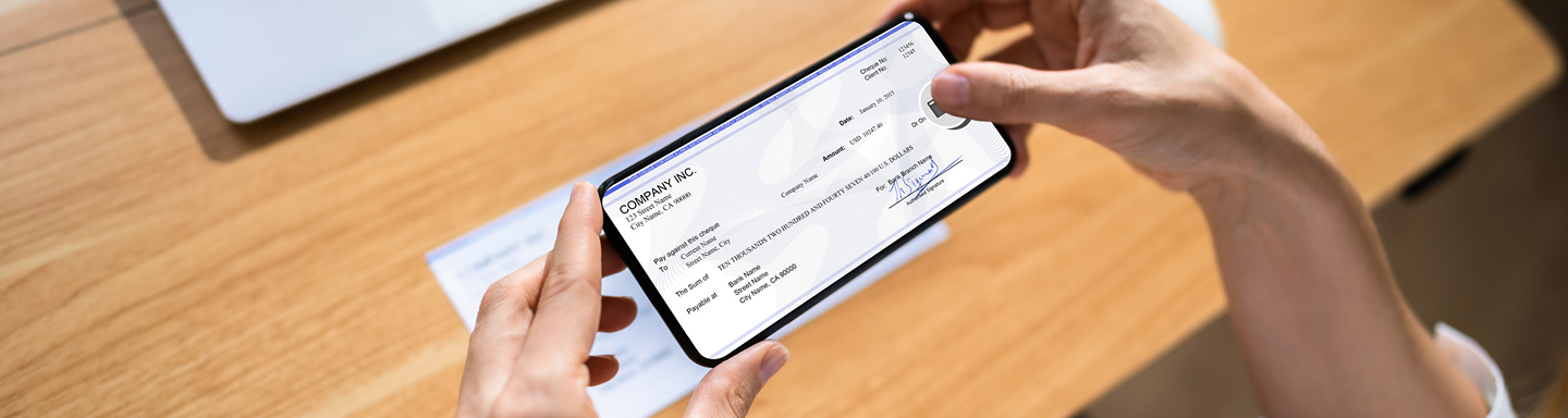 Person holding a smartphone displaying a digital check for mobile deposit over a wooden table.