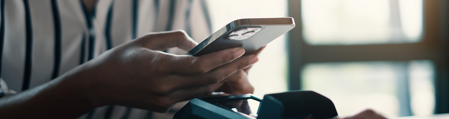 Person holding a smartphone near a card payment terminal, suggesting mobile payment.