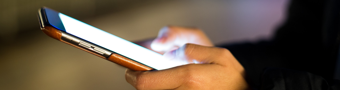 Close-up of hands holding and using a smartphone with a glowing screen in low light.