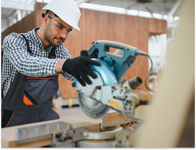 Male carpenter wearing safety gear operating a circular saw to cut wood indoors.