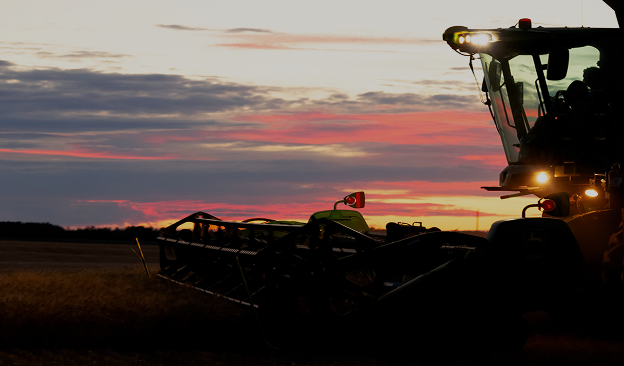 Silhouette of a combine harvester working in a field during a colorful sunset.