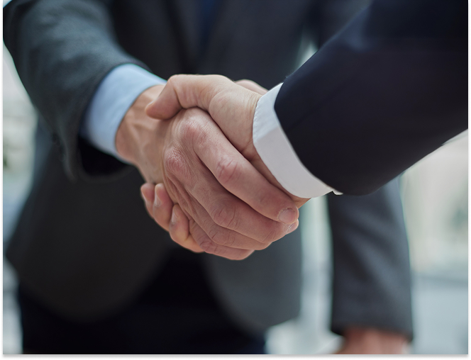 Close-up of two people shaking hands wearing business suits.