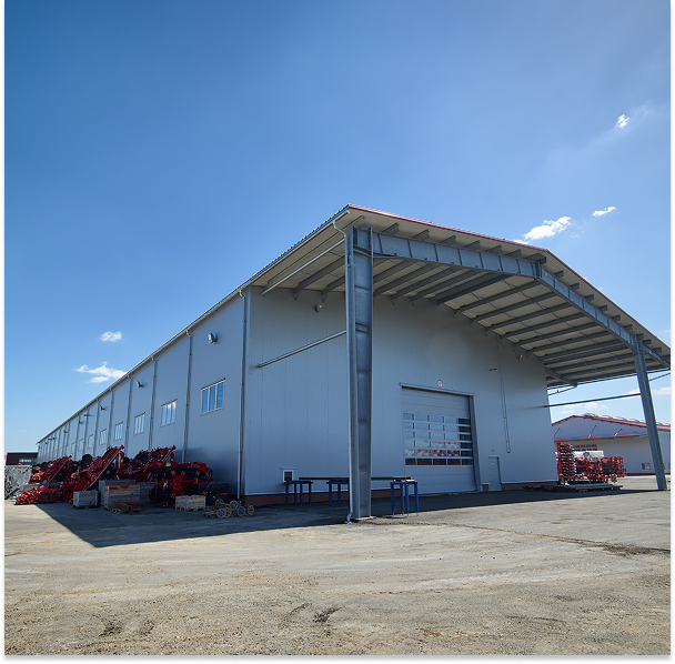 Large industrial warehouse building with metal siding and a covered loading area under a clear blue sky.