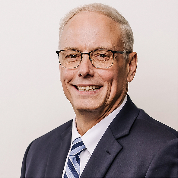 Middle-aged man in a gray suit, white shirt, and red tie smiling against a neutral background.