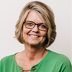 Smiling middle-aged woman with short blonde hair wearing glasses and a dark top against a plain backdrop.