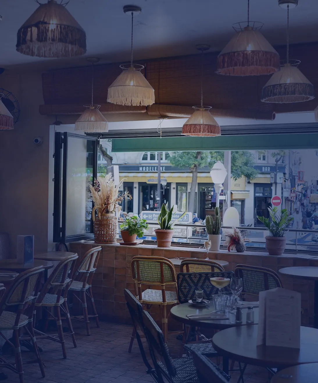 Vue intérieure de la brasserie Marie Belle avec tables en bois, suspensions et vue sur la rue depuis de grandes fenêtres