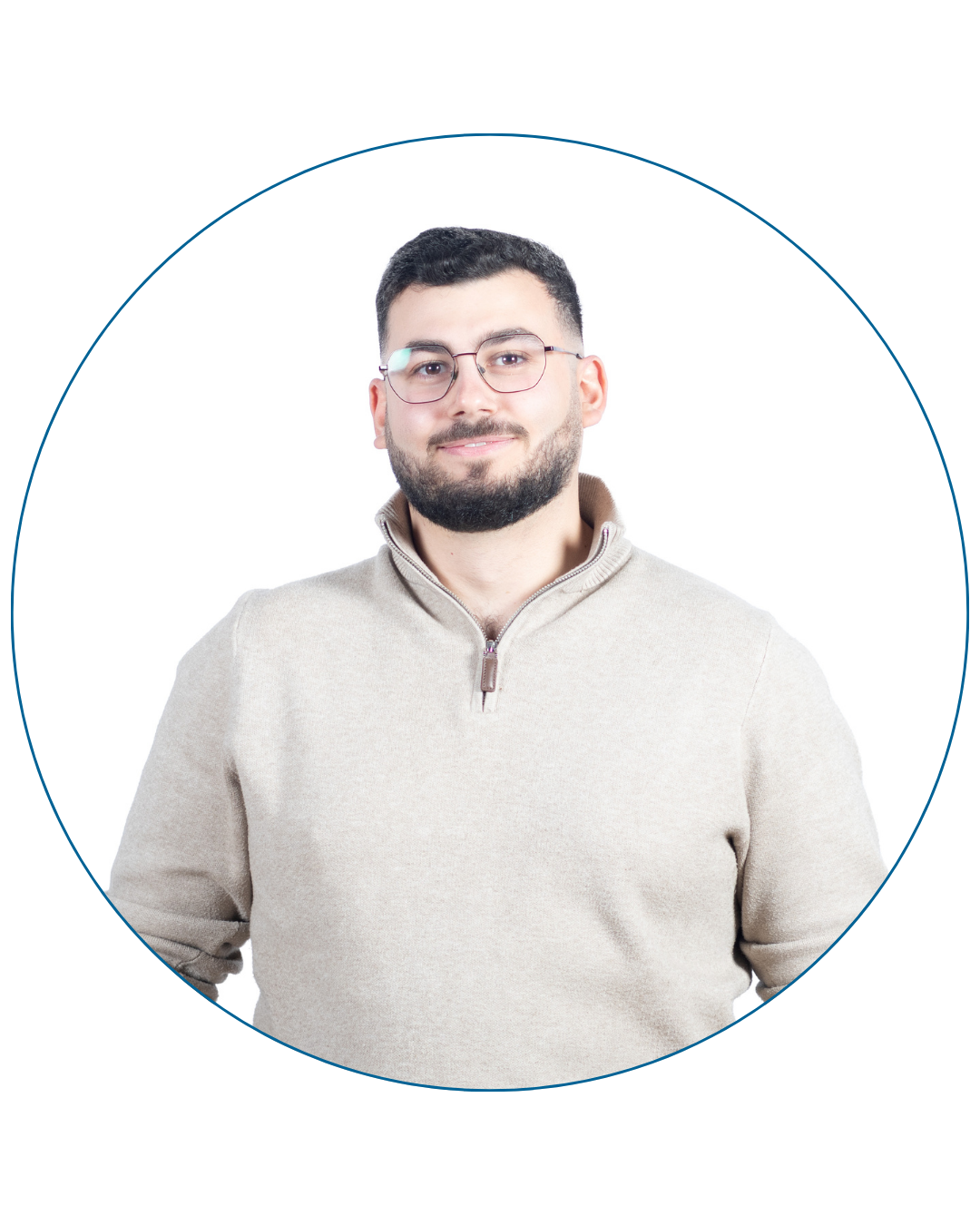 Young man with short dark hair, beard, and glasses wearing a beige zip-up sweater, smiling slightly against a white background.