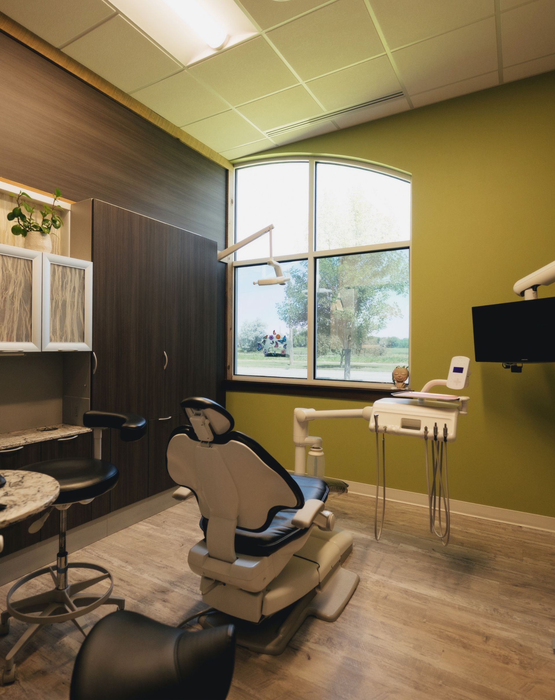 Modern dental office with a black and white dental chair facing a large window with a view of trees and greenery.