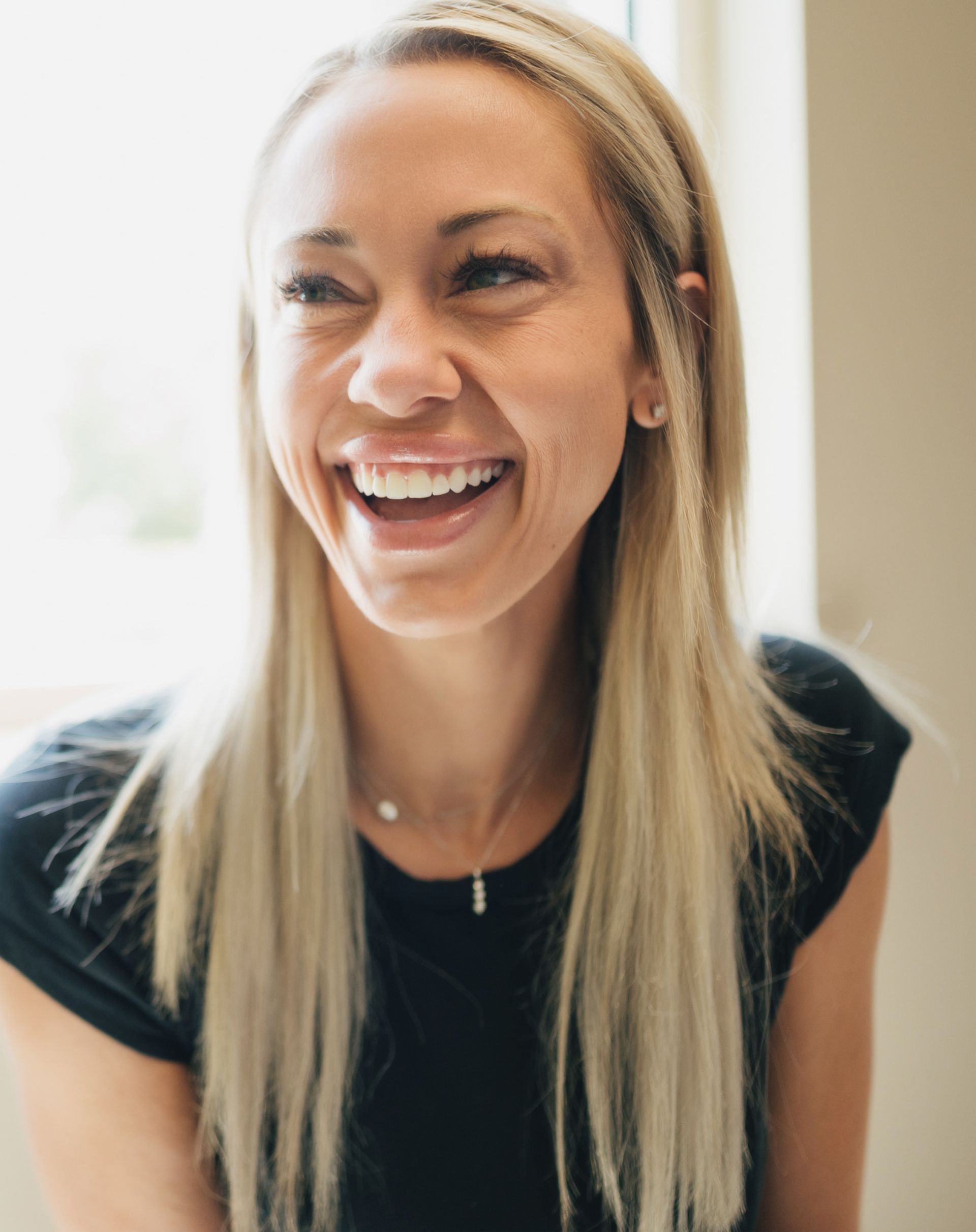 Smiling woman with long blonde hair wearing a black shirt and a necklace.