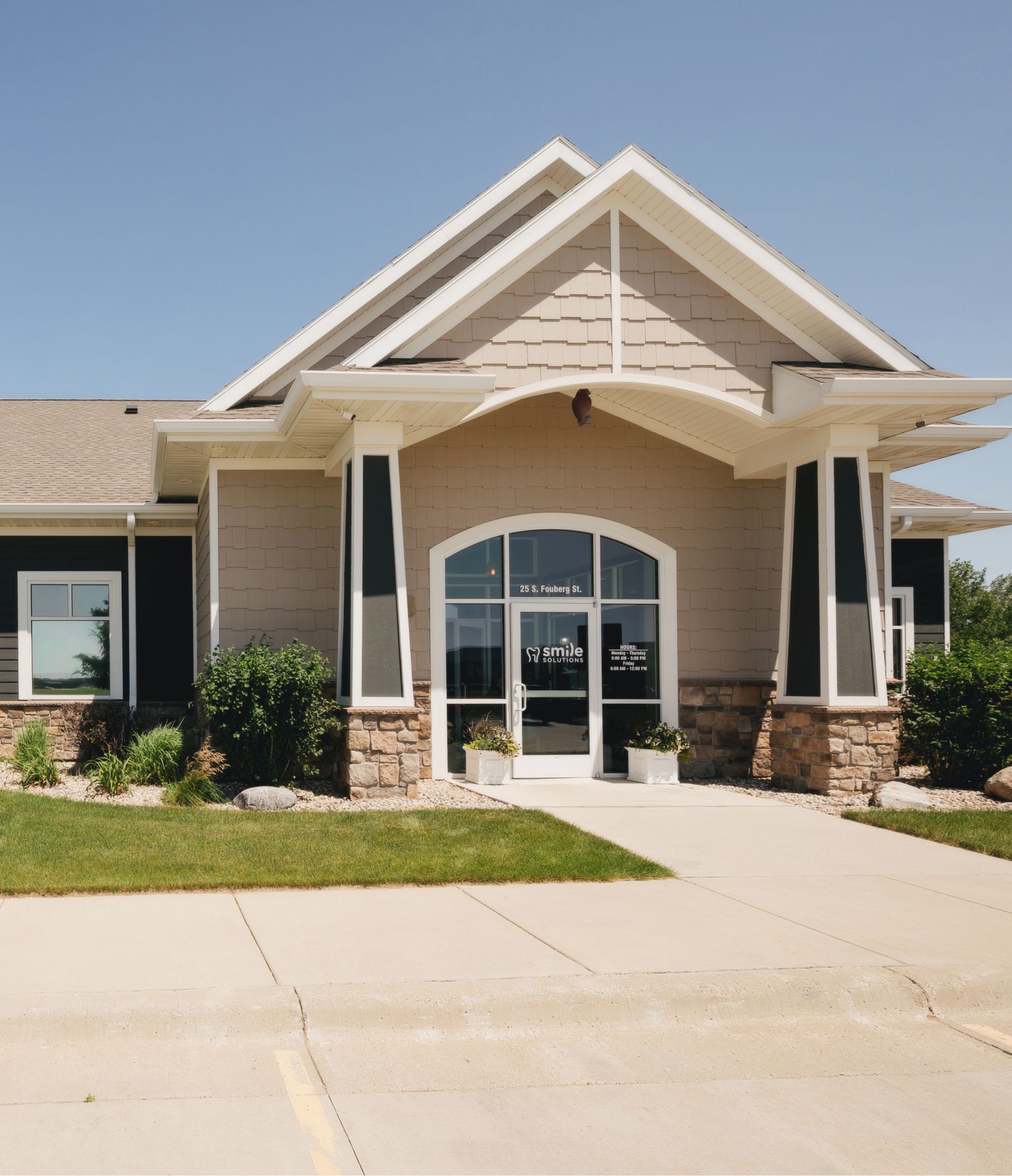 Modern building entrance with arched doorway, stone pillars, and a sign for Smile Solutions dental office.