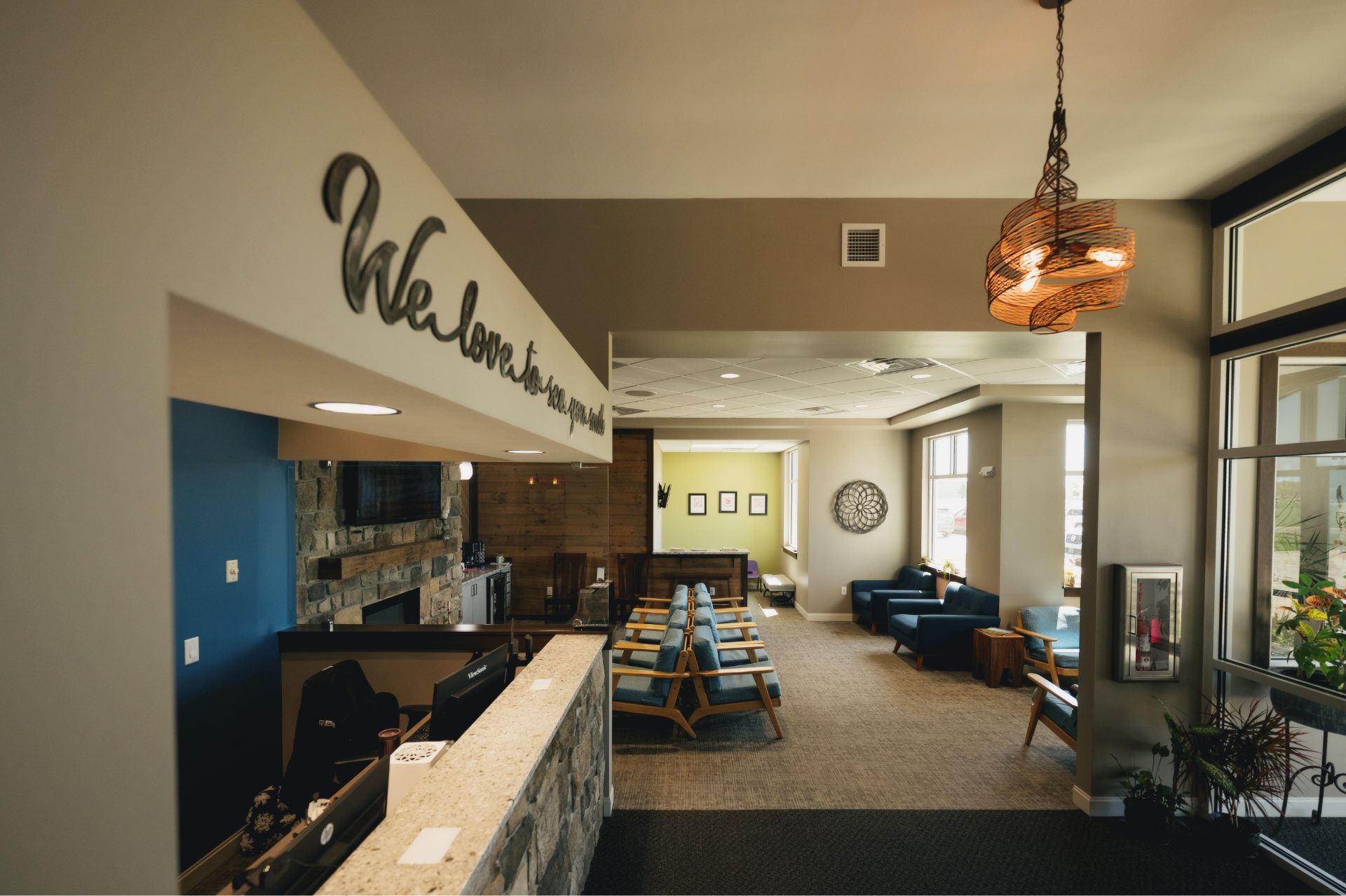 Waiting area with blue cushioned chairs, stone reception desk, and decorative wall sign reading 'We love to see you smile.'