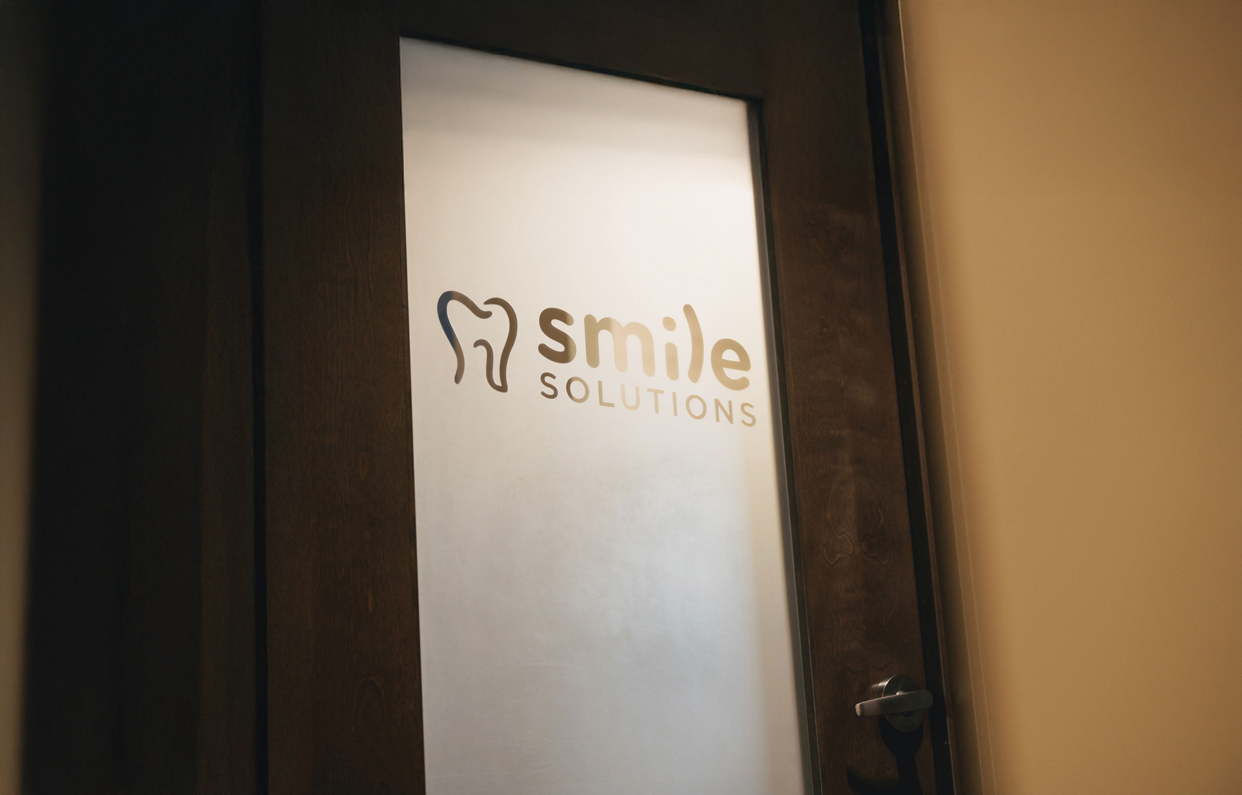 Frosted glass door with a tooth logo and the words 'Smile Solutions' on it.