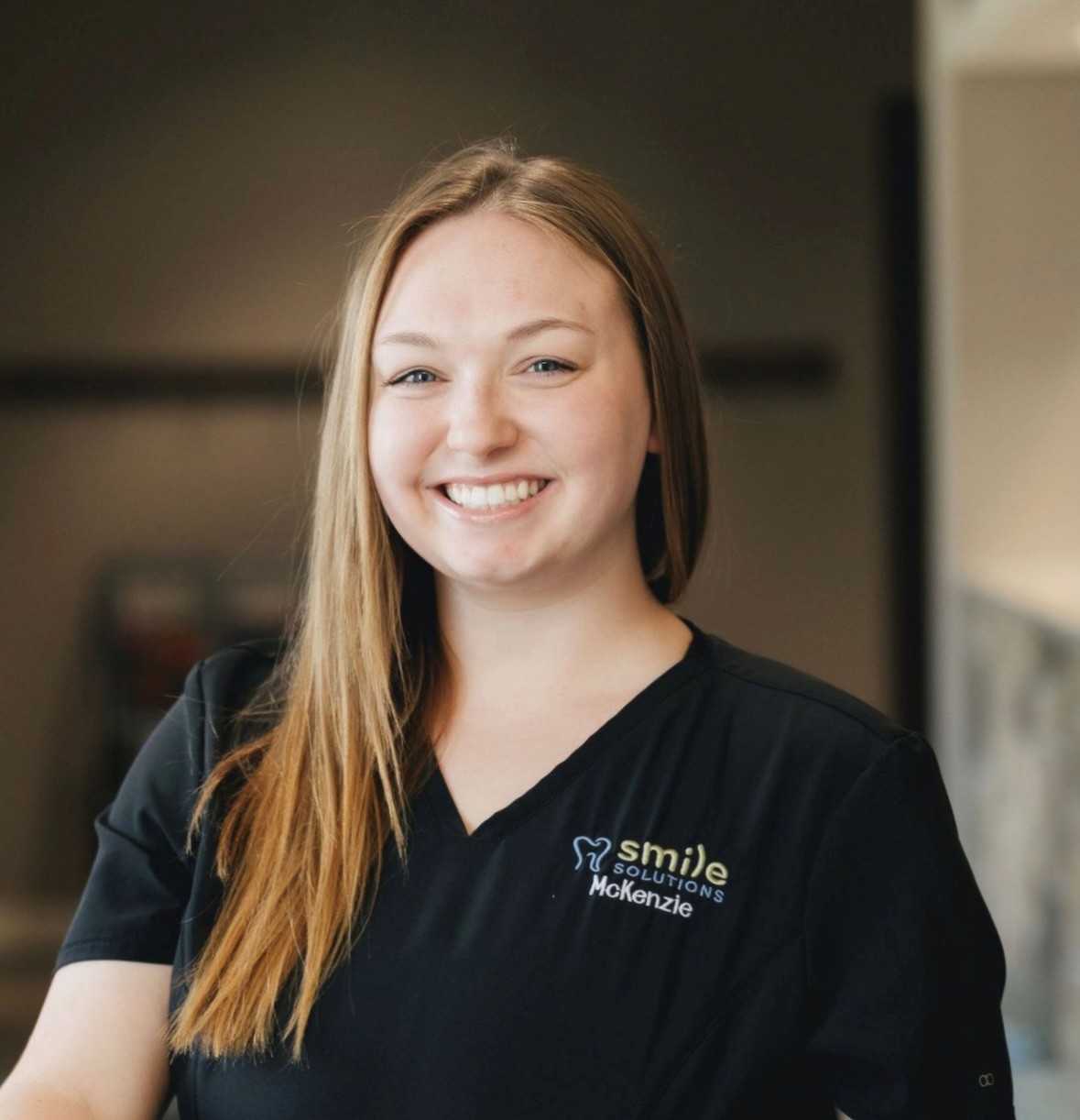 Smiling woman with long blonde hair wearing a black shirt with 'Smile Solutions McKenzie' logo.