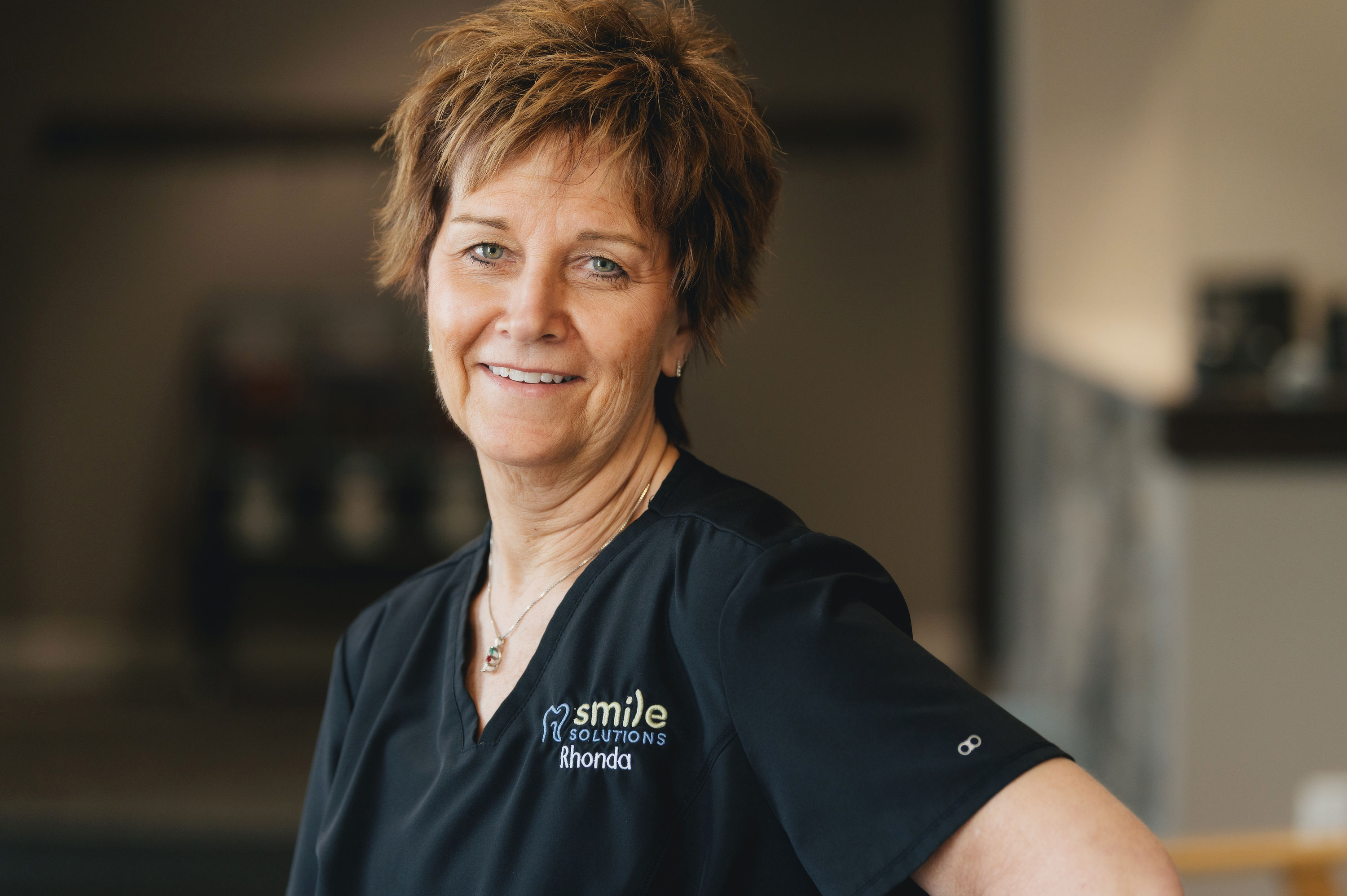Smiling woman wearing a black Smile Solutions uniform with the name Rhonda embroidered.