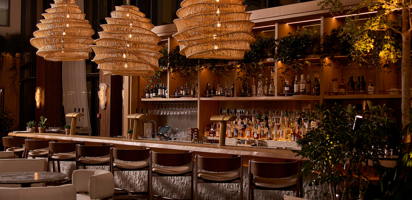 Cozy bar interior with a marble counter, wooden chairs, warm lighting, and bottles on shelves.