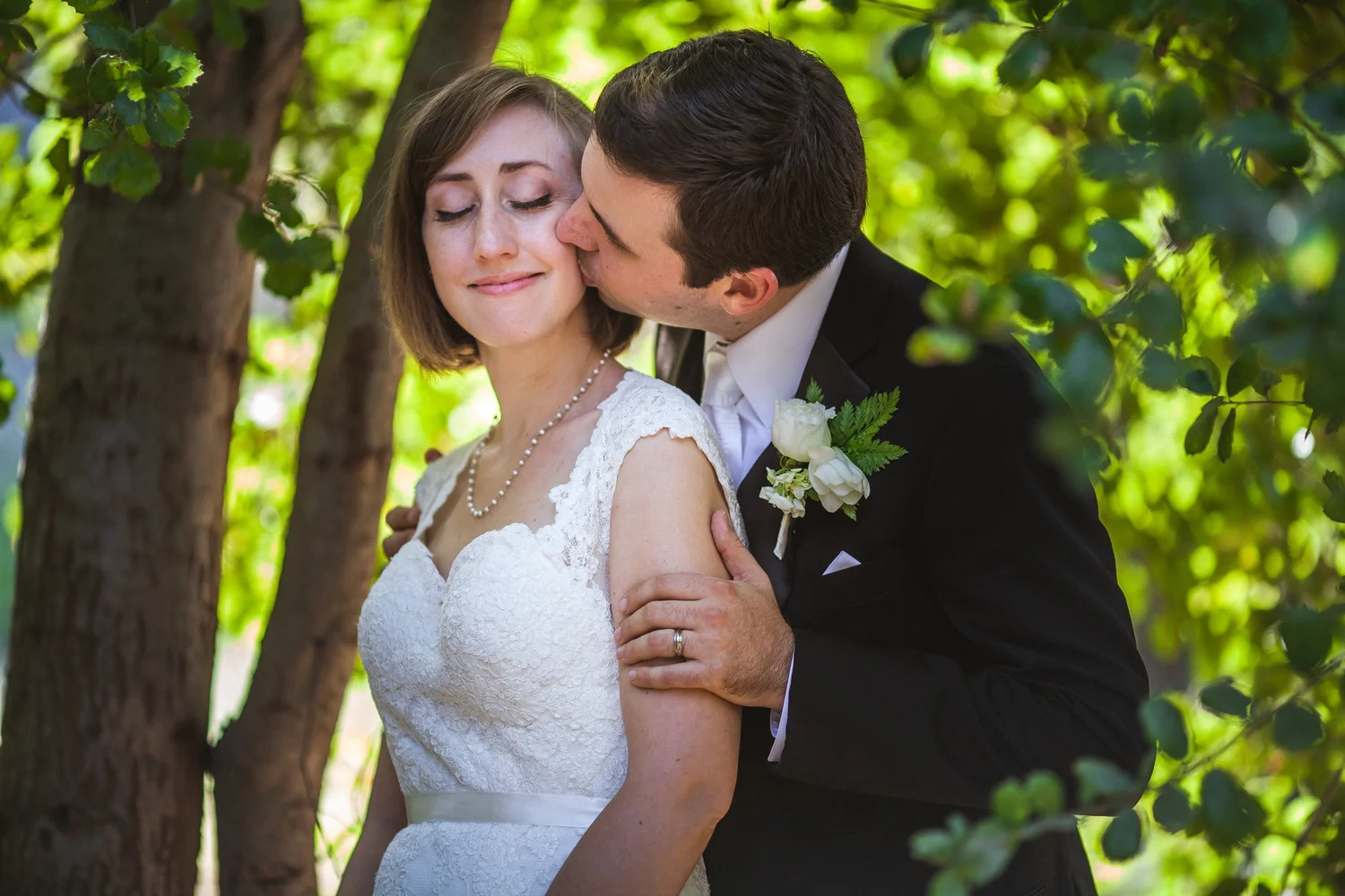 Groom in black suit kissing bride in white lace dress