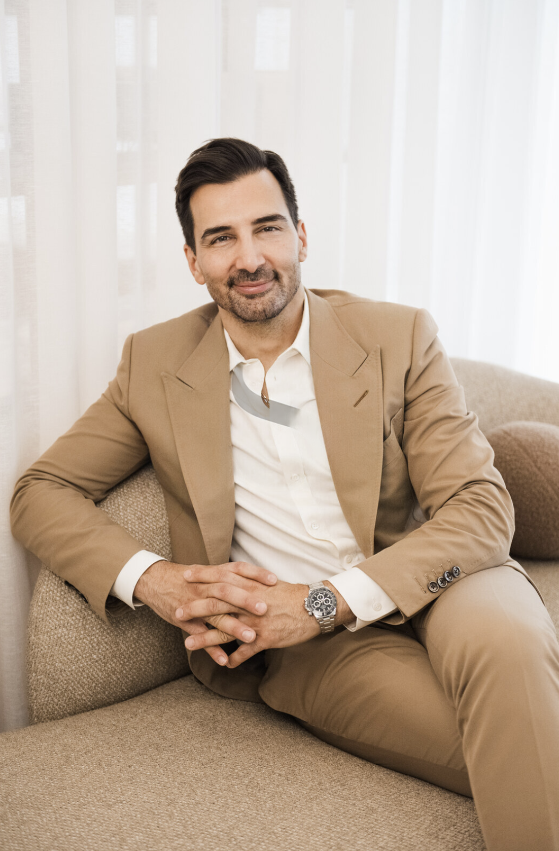 Dr. Motakis sitting on a beige couch with hands clasped.