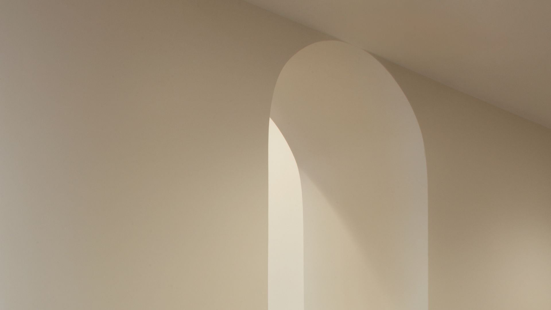 Minimalist beige wall with an arched alcove casting soft shadows.