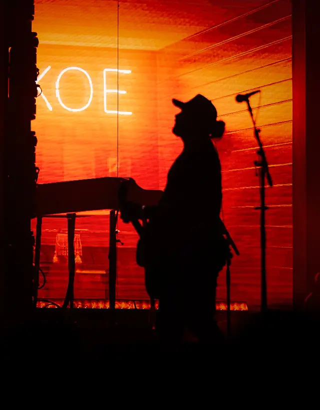 Koe Wetzel silhouetted against a neon sign spelling out KOE
