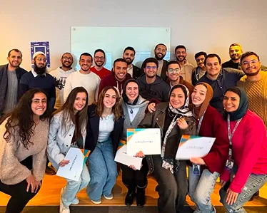 Group of smiling young adults posing indoors, some holding certificates, in a casual setting.
